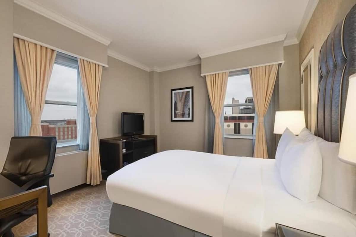 A hotel room with a bed, a desk, a television, and a window with curtains.