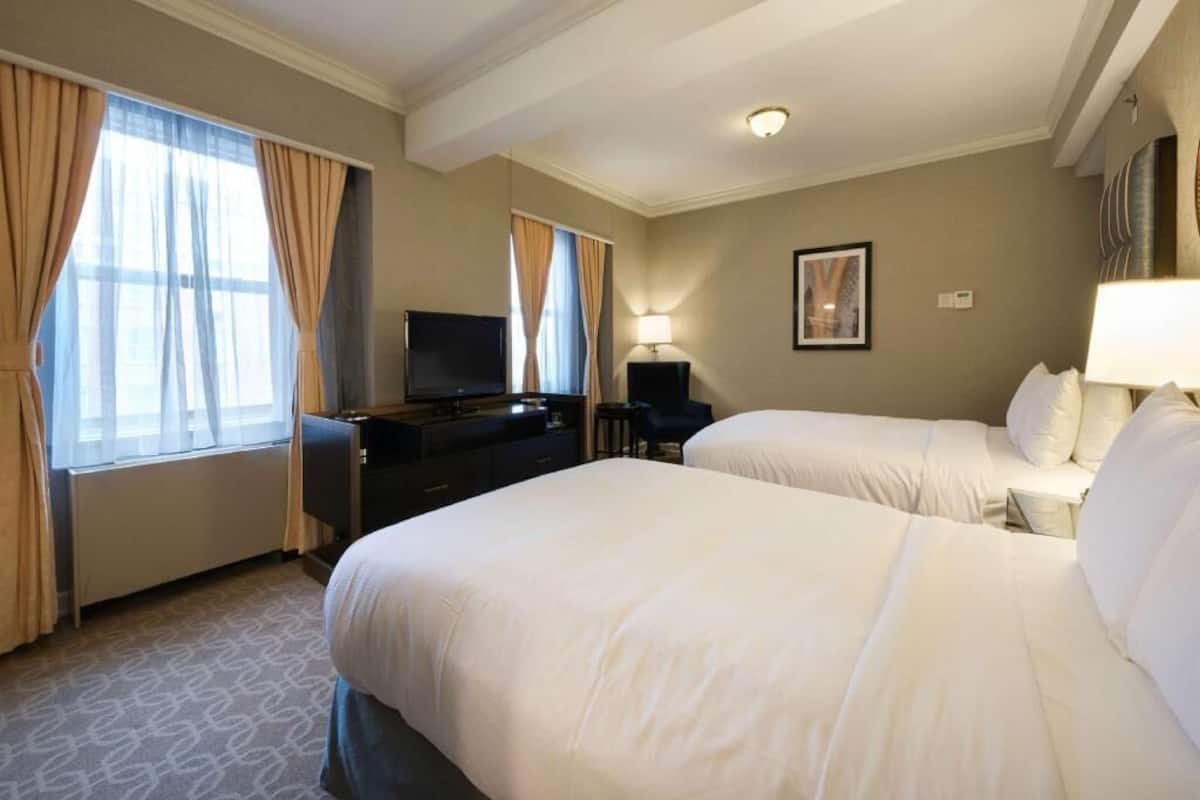 A hotel room with two beds, a TV, a desk, and a lamp.
