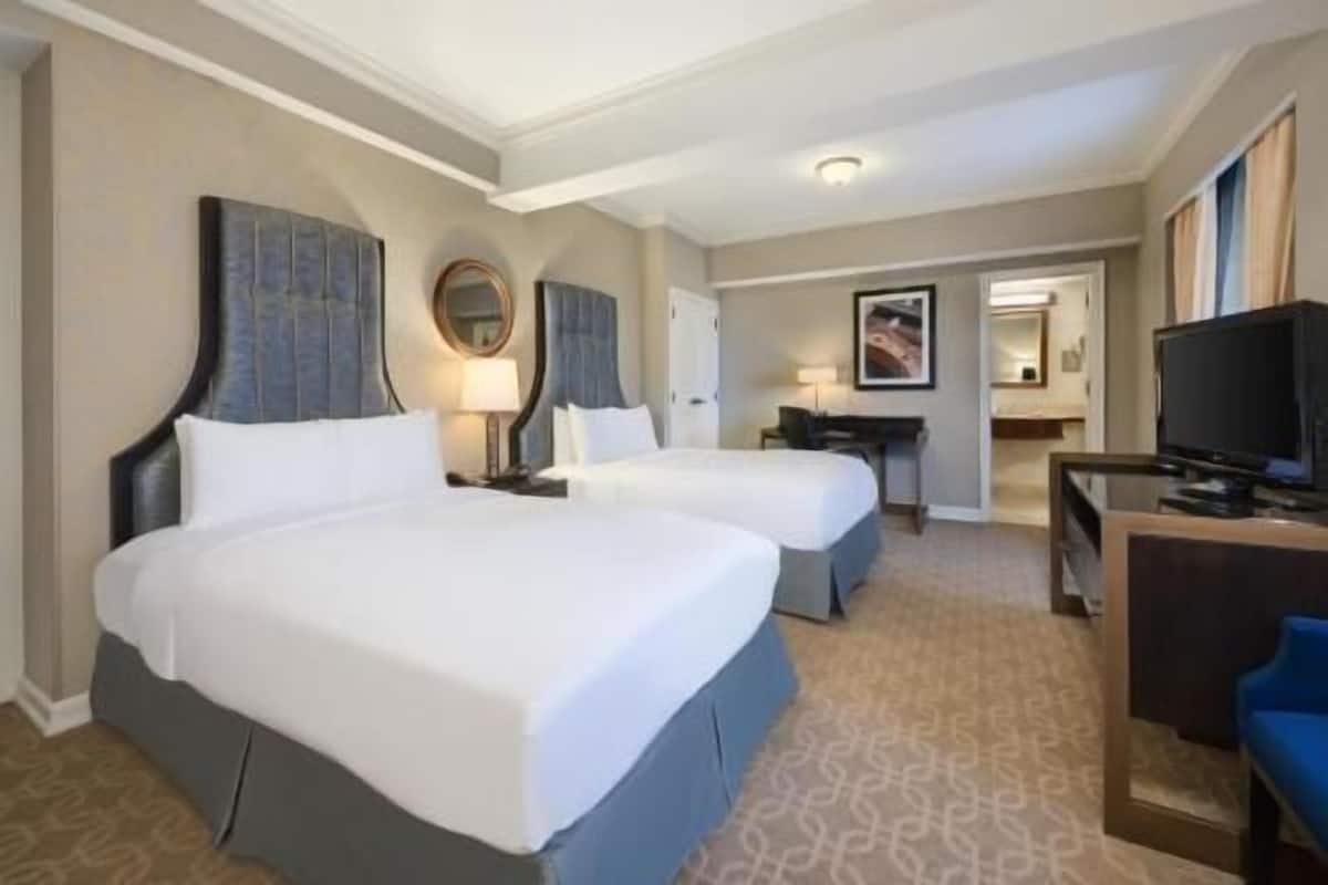 A hotel room with two beds, a desk, a TV, and a mirror.