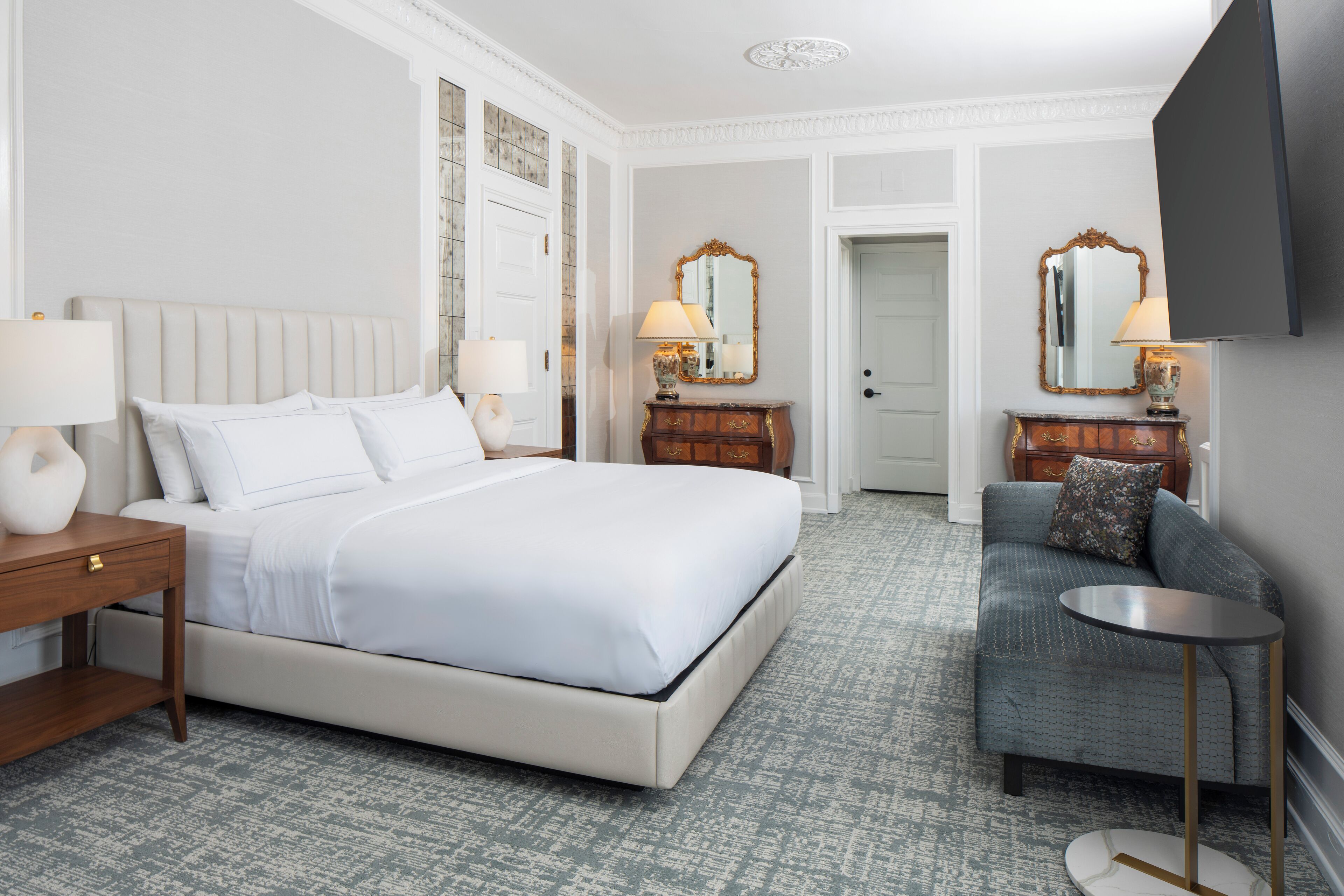 A hotel room with a large bed, a sofa, a small table, and two lamps.