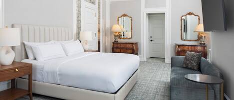 A hotel room with a large bed, a sofa, a small table, and two lamps.