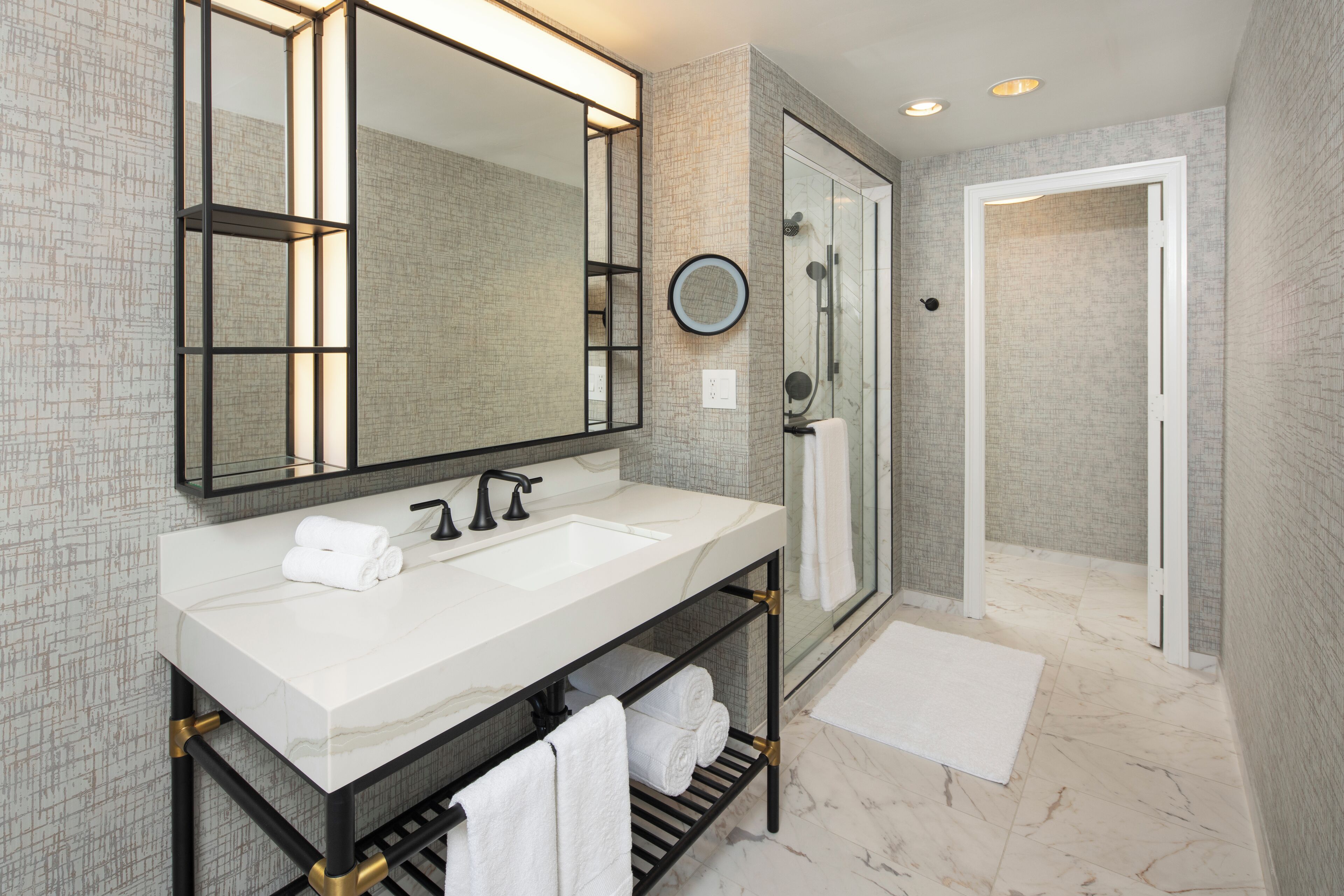A modern bathroom with a large mirror, dual sinks, and a walk-in shower.