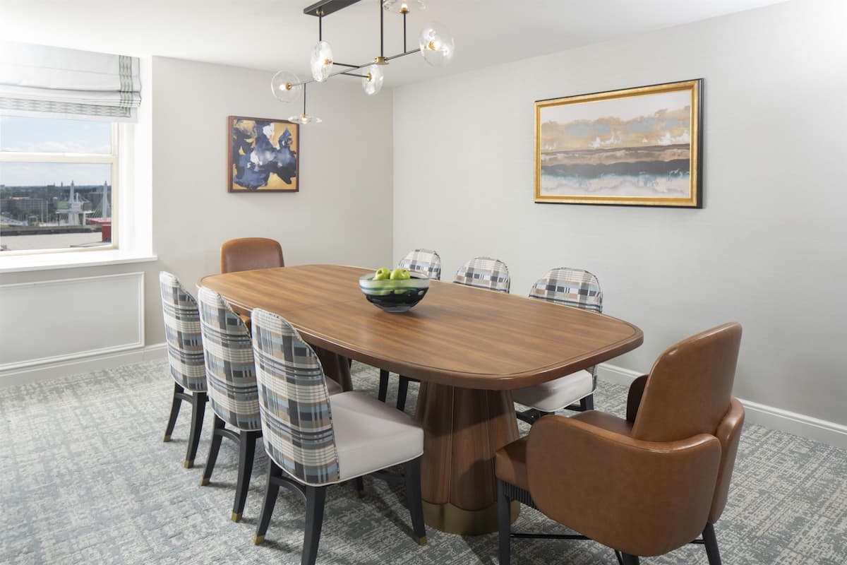 A dining room with a wooden table, plaid chairs, a bowl of fruit, and artwork on the walls.