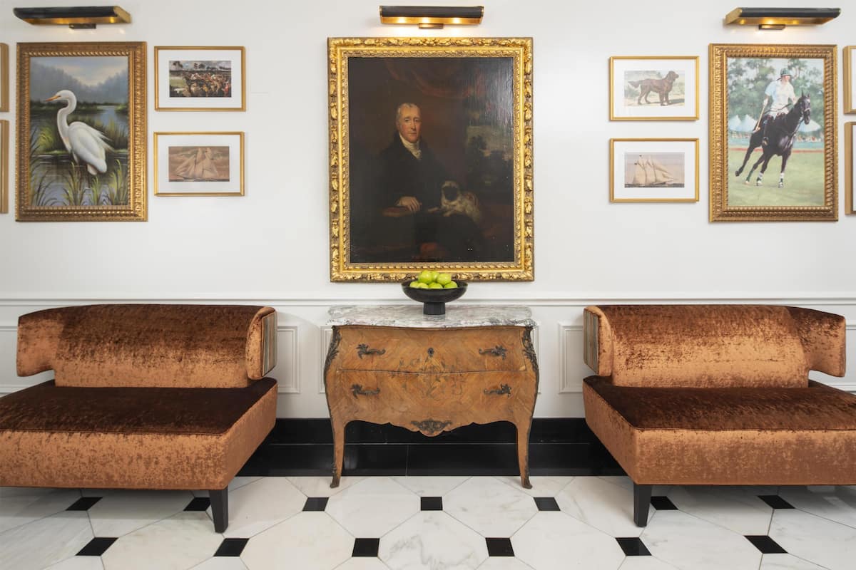 A room with two velvet sofas, a central table with a bowl of fruit, and framed artwork on the walls.