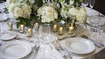 A table set for a formal event with white plates, silverware, and clear glassware, accompanied by small candles and a floral centerpiece.