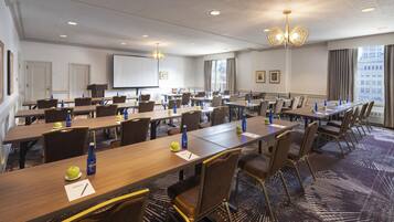 A conference room with multiple tables, chairs, and a projector screen.