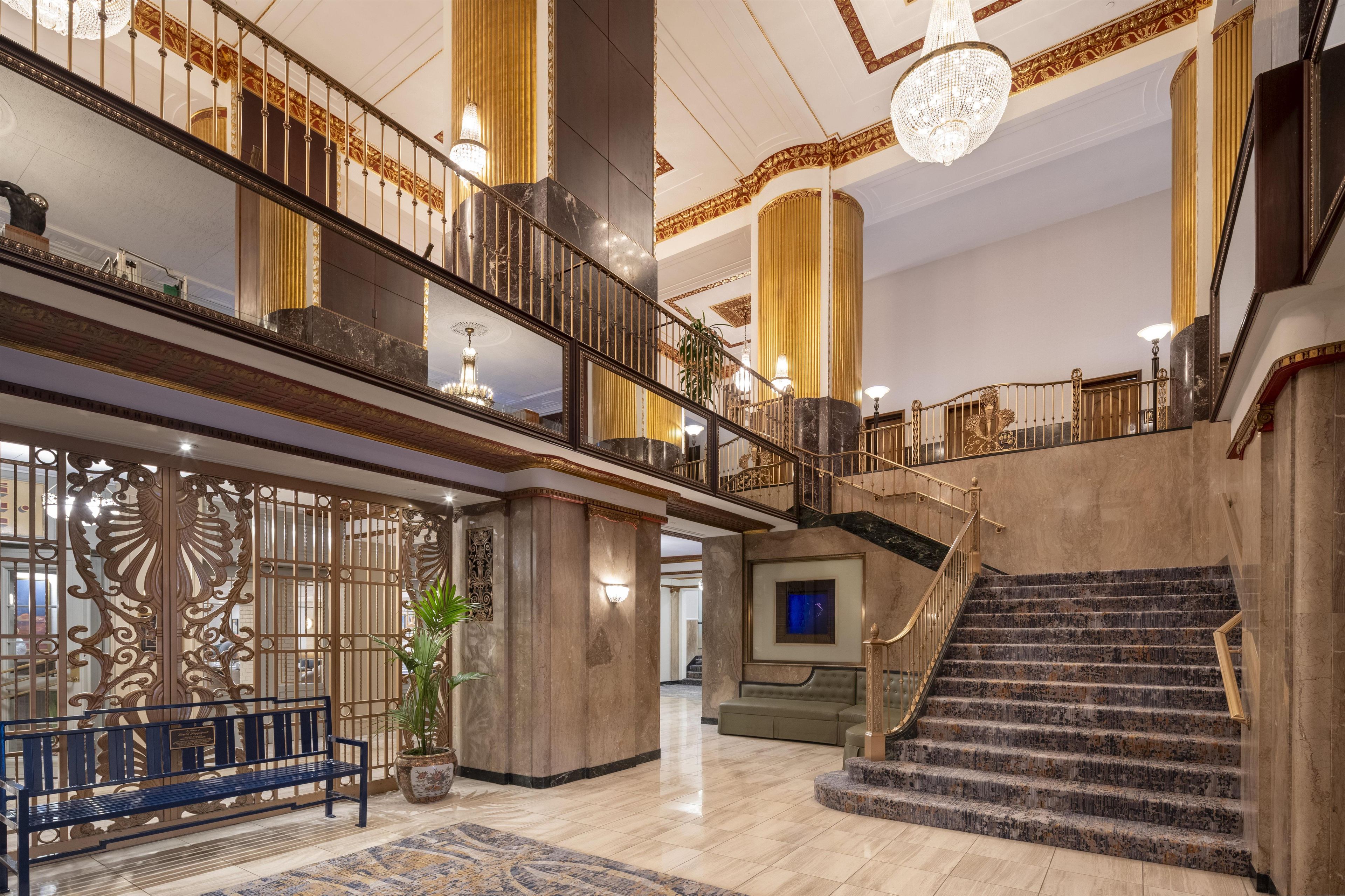 A grand lobby with a marble staircase, a bench, and a decorative wall.