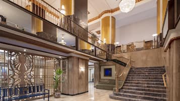 A grand lobby with a marble staircase, a bench, and a decorative wall.