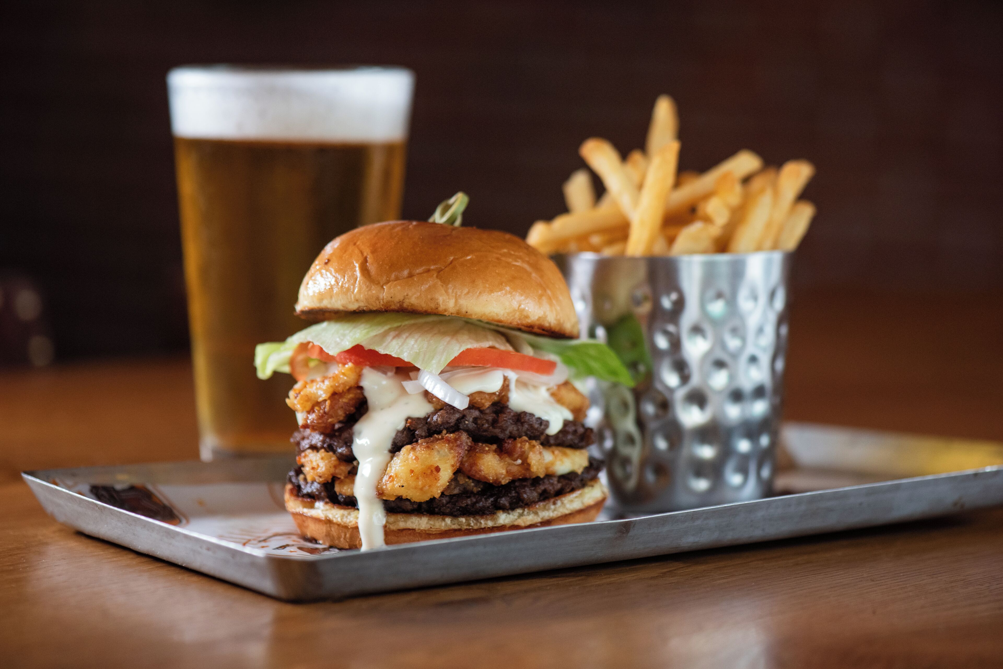 A burger with fries and a glass of beer on a tray.
