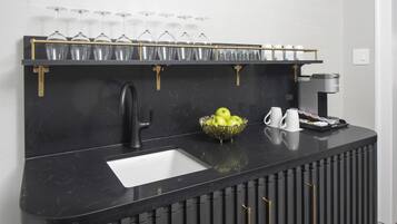 A black marble bar with a sink, a coffee machine, a bowl of apples, and a wine glass rack.