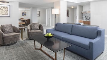 A modern living room with a blue sofa, two armchairs, a coffee table, and a dining area in the background.