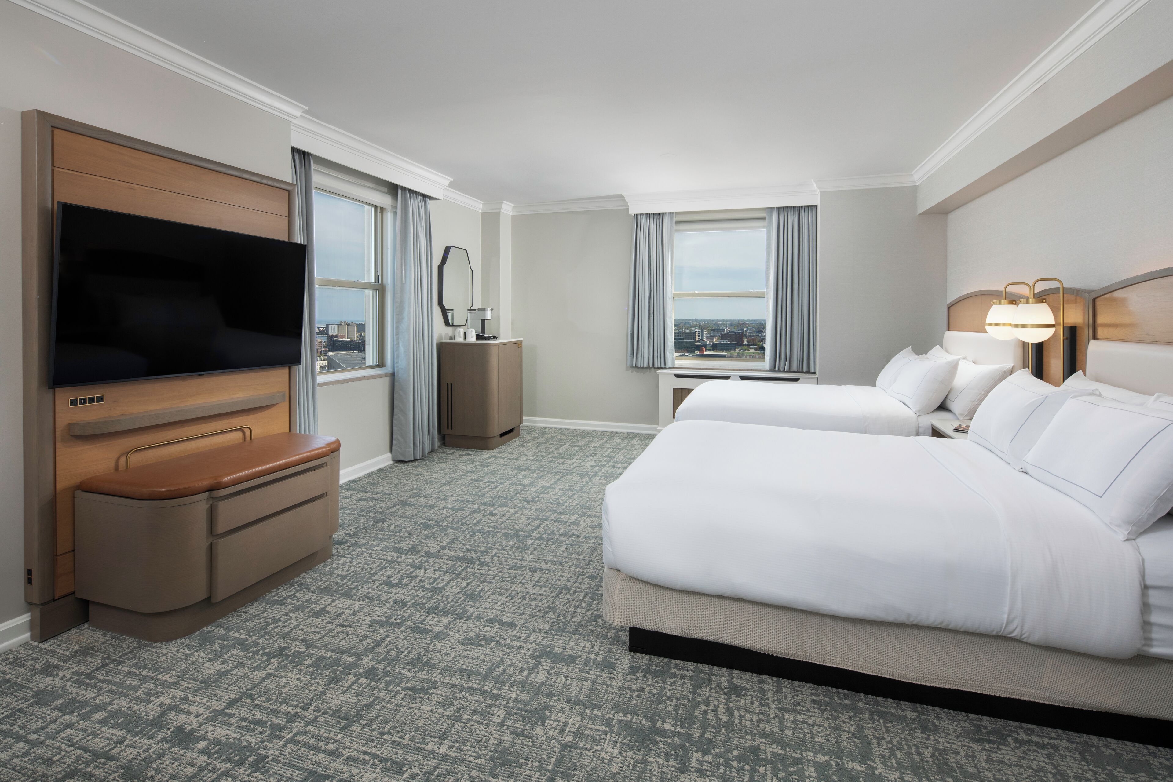 A hotel room with a large flat-screen TV, a sofa, two beds, a desk, and a view of the city.