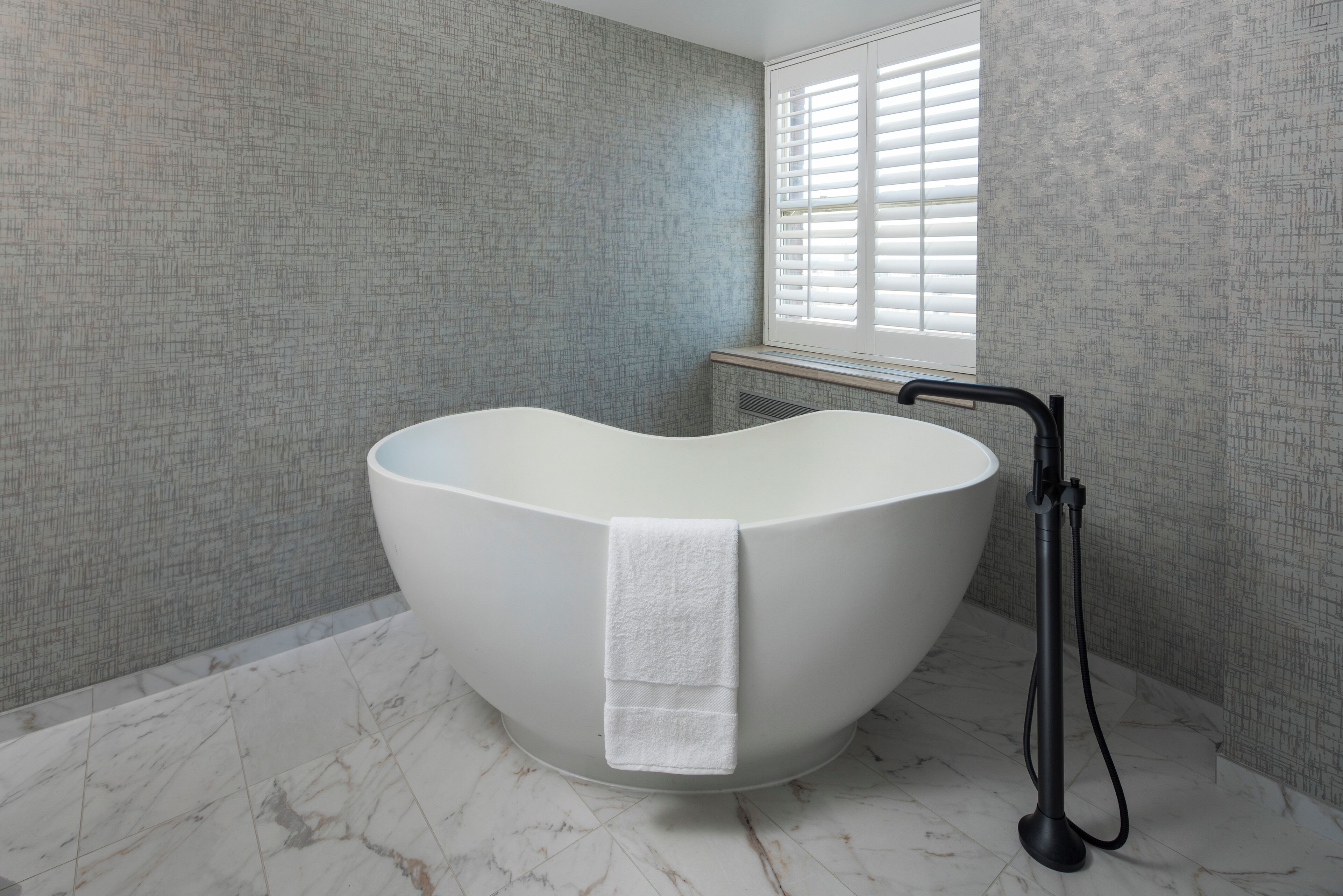 A modern bathroom with a heart-shaped bathtub, a towel hanging on it, and a handheld showerhead.