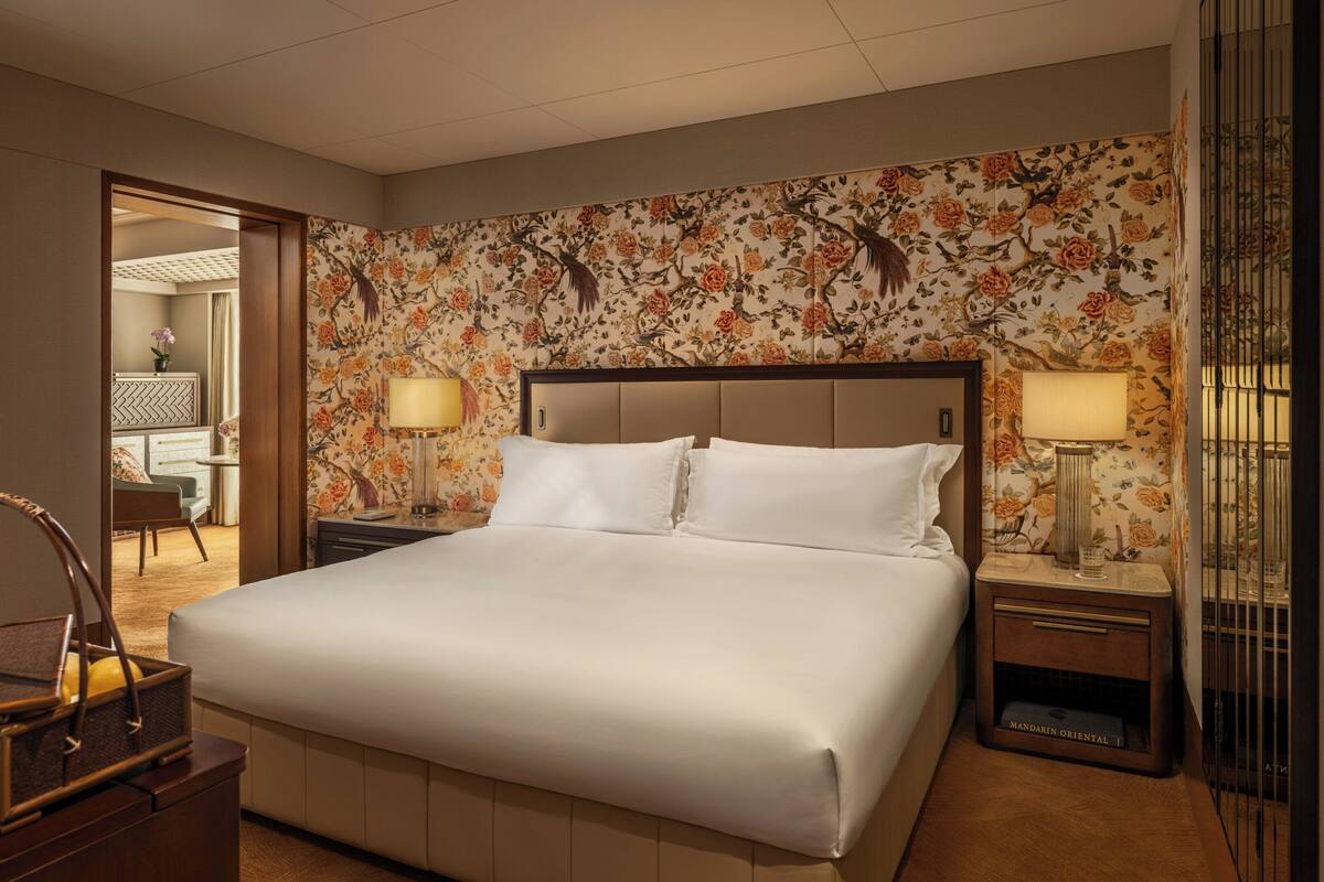 A hotel room with a large bed, two bedside tables with lamps, a wooden nightstand, a chair, and a mirror.
