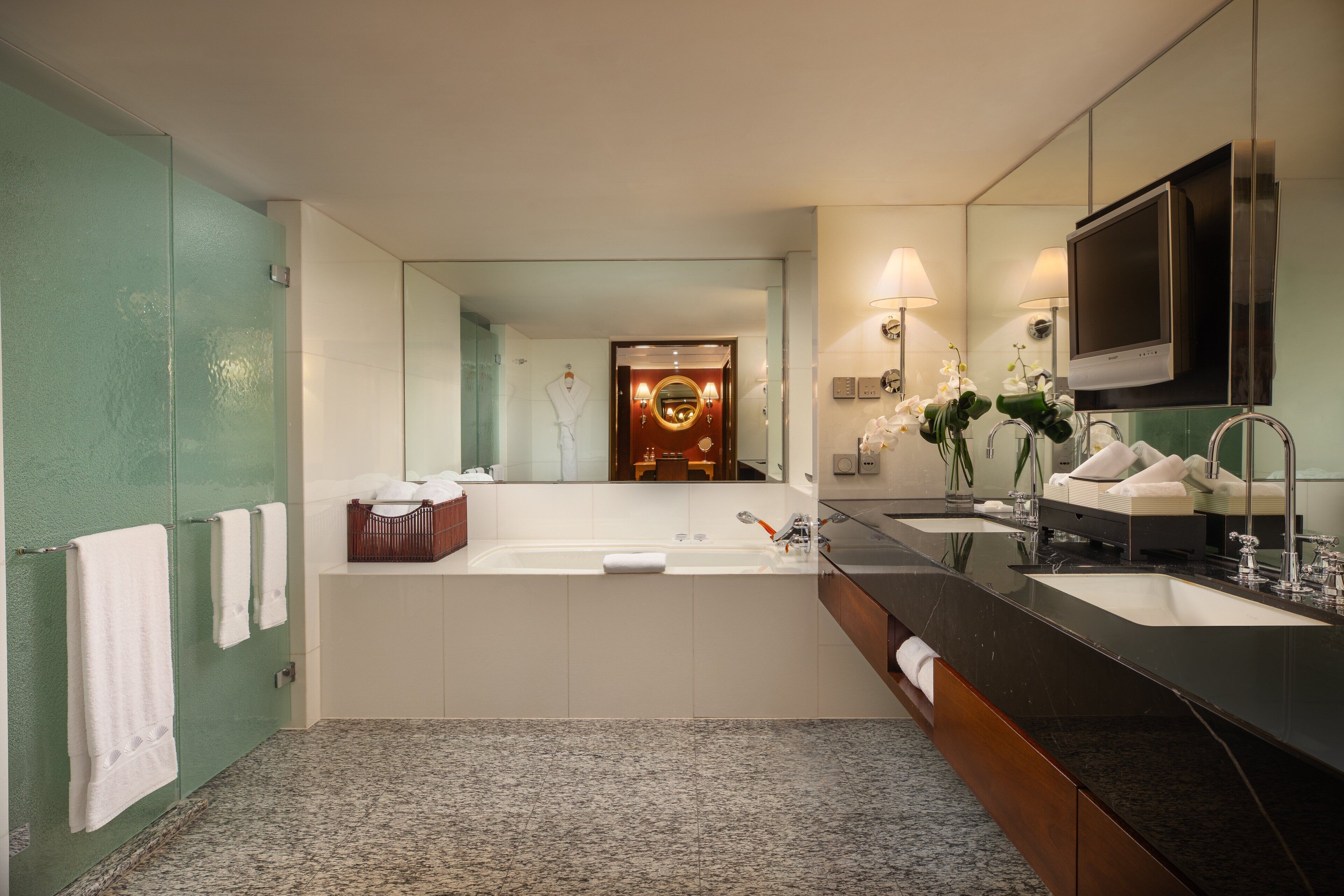 Un baño moderno con un espejo grande, dos lavamanos, una bañera y un tocador con televisor.