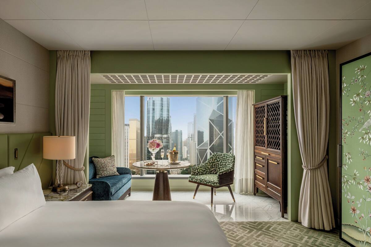 A hotel room with a bed, a seating area with a table, a view of the cityscape, and a large window.