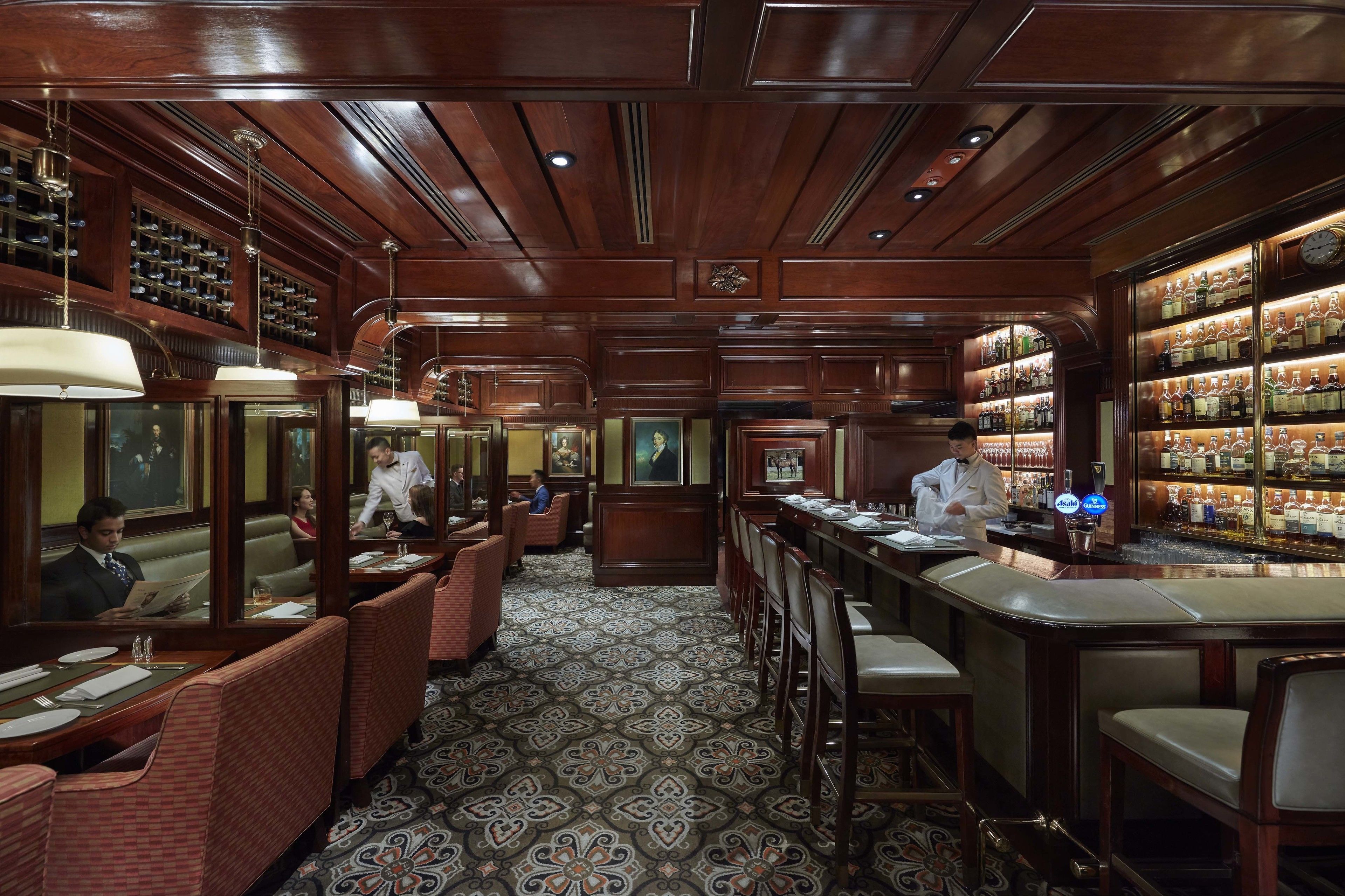 A classic bar area with wooden paneling, a patterned floor, and a bartender at the counter.