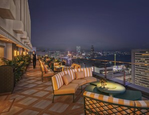Terraza en la azotea con asientos al aire libre, vista al horizonte de la ciudad y un cuerpo de agua al fondo.