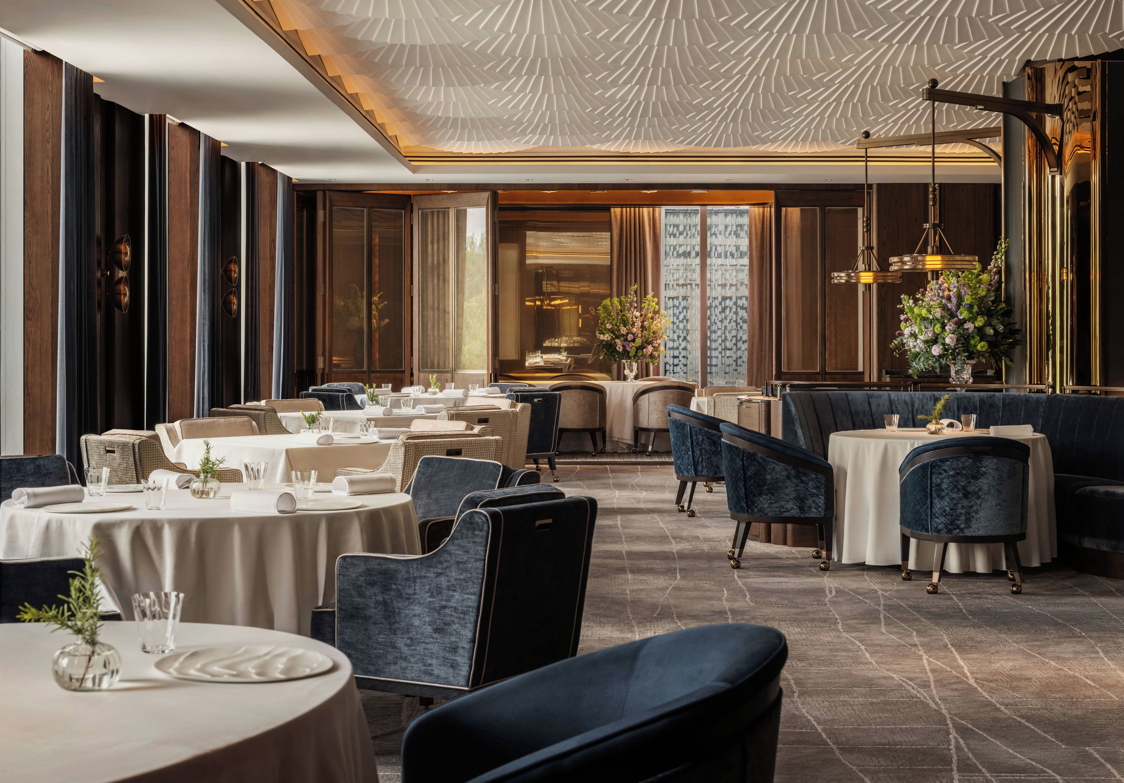 Ein Restaurant mit runden Tischen, blauen gepolsterten Stühlen und einer gemusterten Decke.