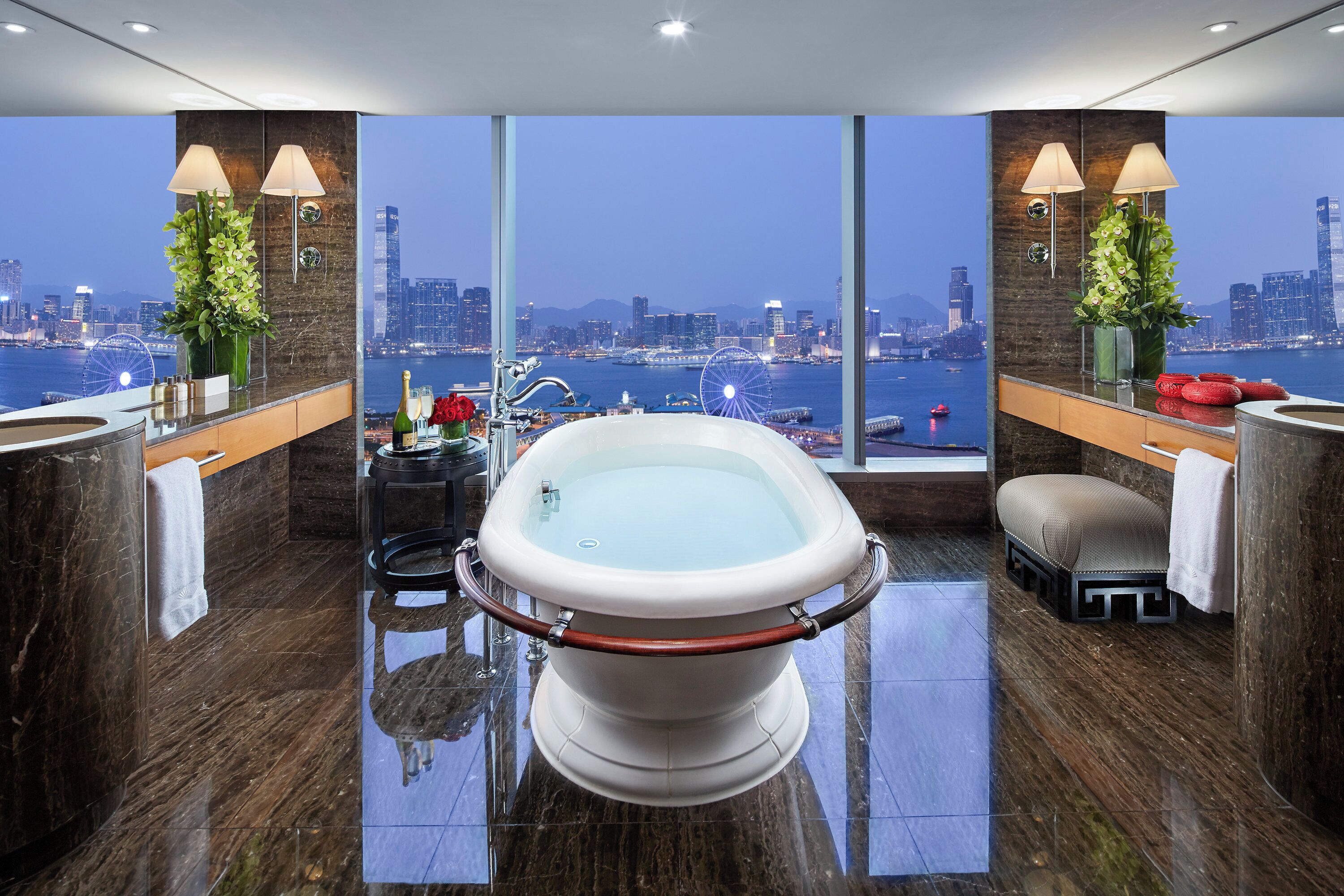 Een moderne badkamer met een groot bad, een wastafel met spiegel en een uitzicht op een stadsbeeld door grote ramen.