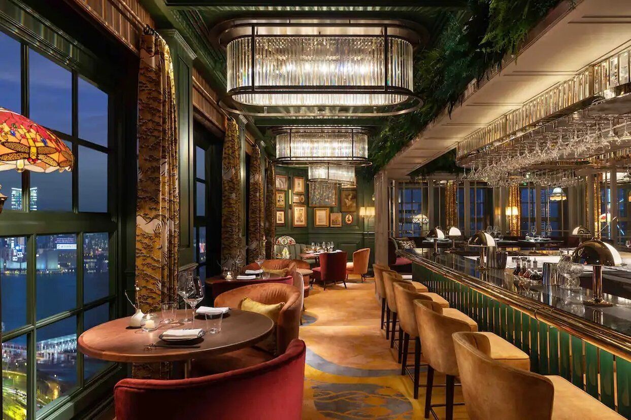 A bar area with seating, a view of the city, and a chandelier.