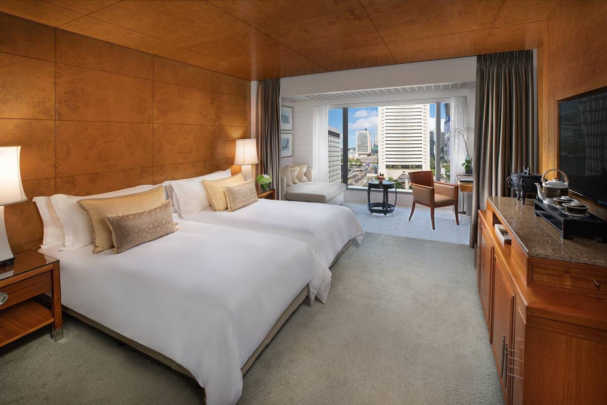 A hotel room with two beds, a desk, a chair, a TV, and a view of the city.