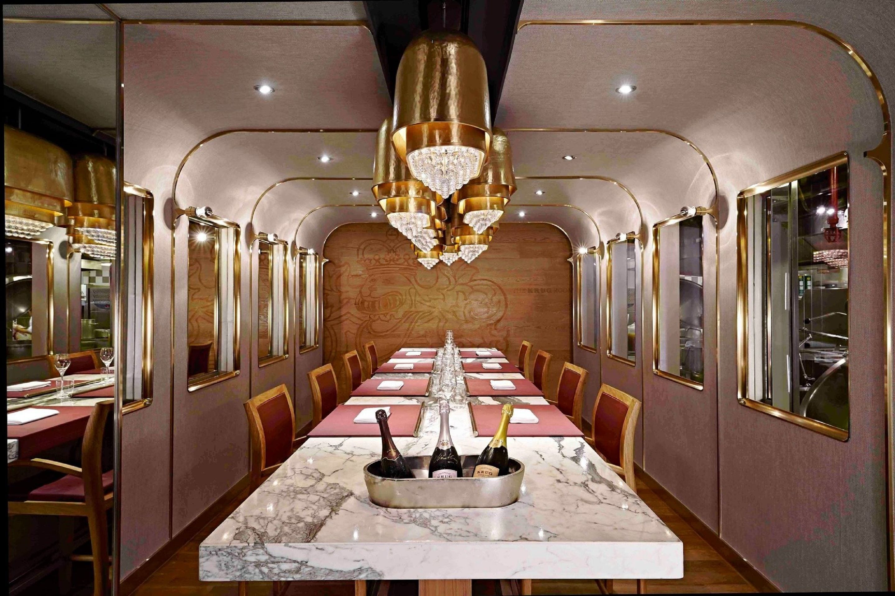 Une longue table à manger, surmontée d’un plateau en marbre, entourée de chaises, et agrémentée d’un centre de table composé de bouteilles de champagne.