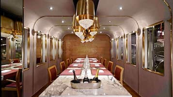 Une longue table à manger, surmontée d’un plateau en marbre, entourée de chaises, et agrémentée d’un centre de table composé de bouteilles de champagne.