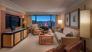A modern hotel room with a large TV, comfortable seating, a coffee table, and a view of a cityscape and body of water. - Mandarin Oriental, Hong Kong (Hong Kong)