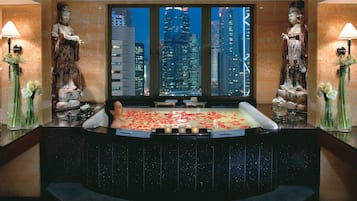 A spa area with a hot tub, two statues, and a city view through large windows.