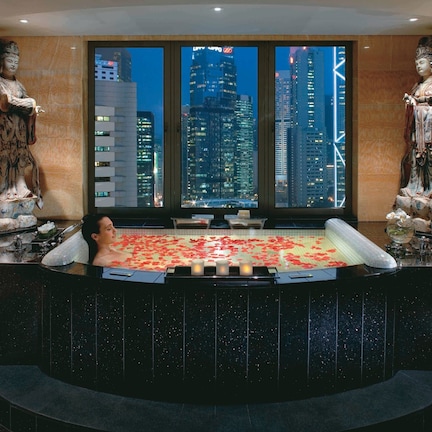 A spa area with a hot tub, two statues, and a city view through large windows.