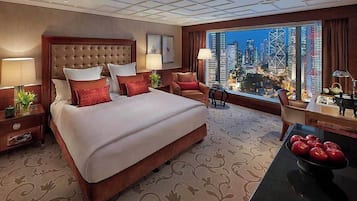 Ein Hotelzimmer mit einem großen Bett, zwei Stühlen, einem Tisch mit Äpfeln und Blick auf die Stadt.