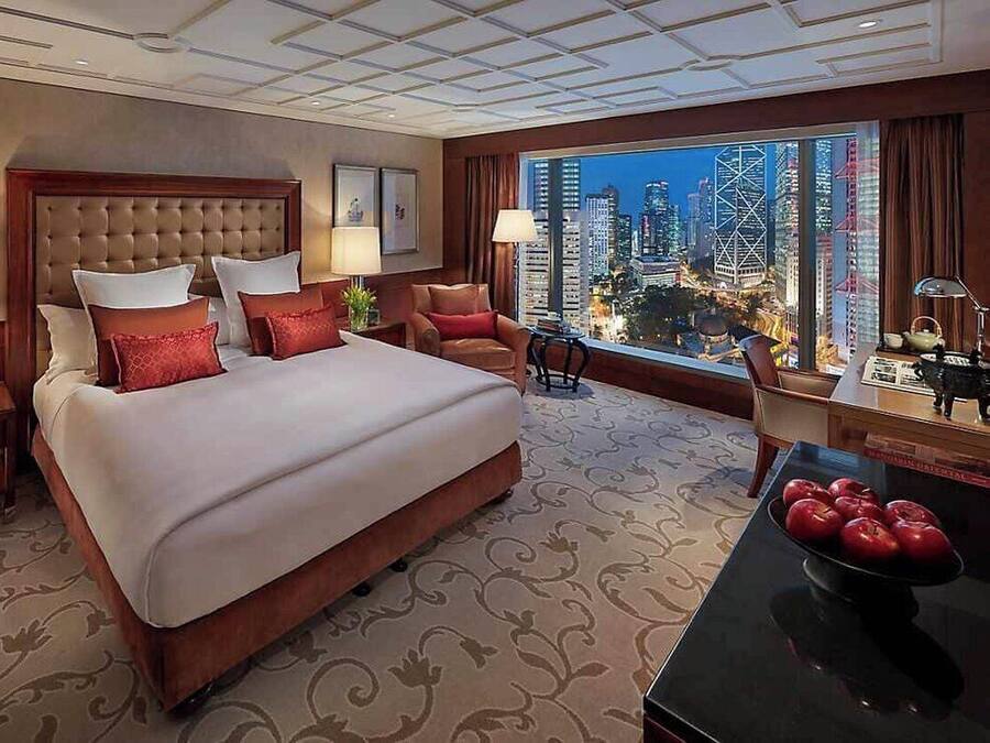 Ein Hotelzimmer mit einem großen Bett, zwei Stühlen, einem Tisch mit Äpfeln und Blick auf die Stadt.