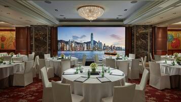 A conference room with round tables, white chairs, and a large screen displaying a cityscape view.