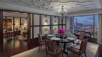 A dining area with a round table set for four, surrounded by wooden chairs, with a cityscape view through large windows.