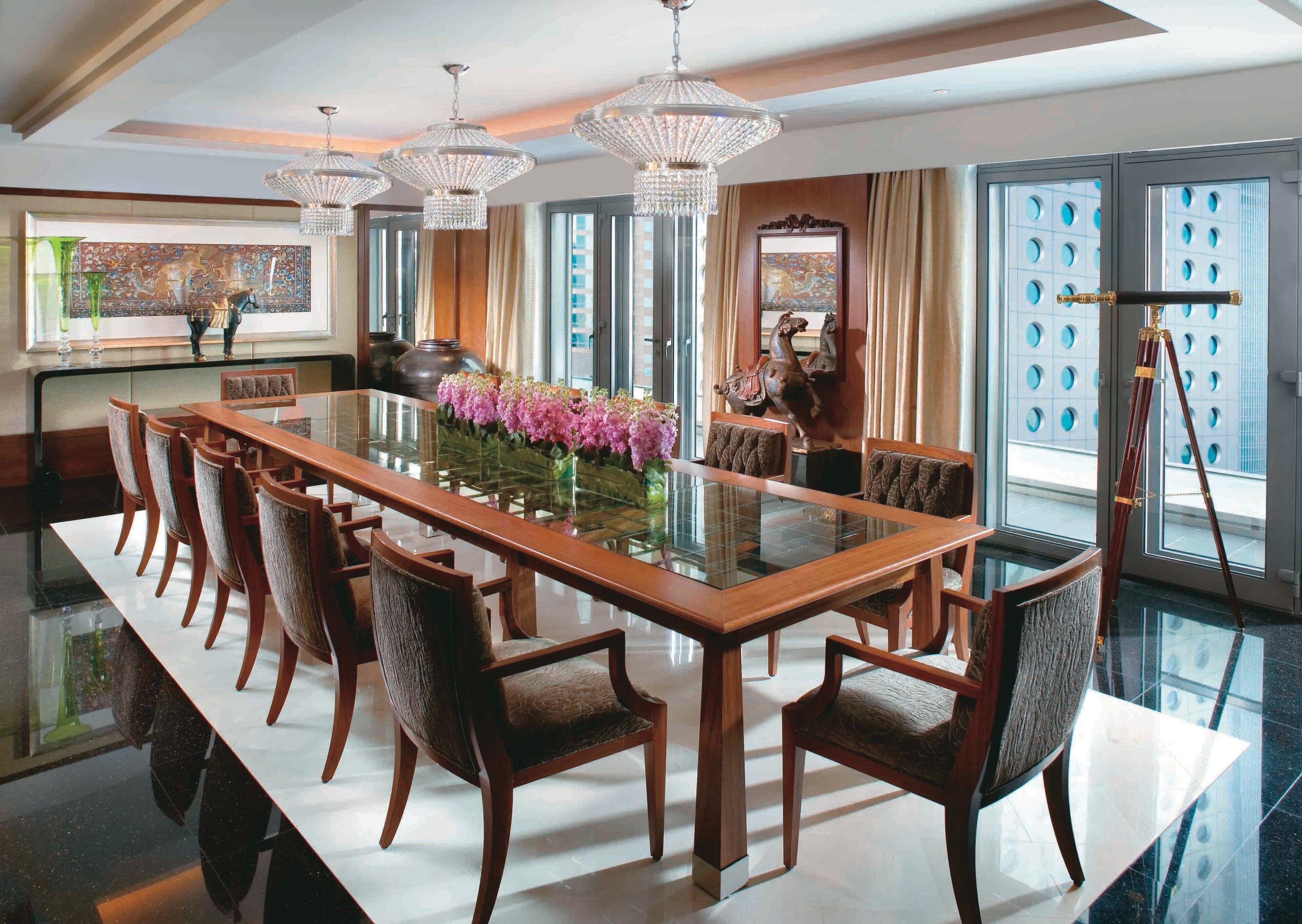 Un comedor espacioso con una larga mesa de madera, sillas elegantes y una mesa con cubierta de vidrio.