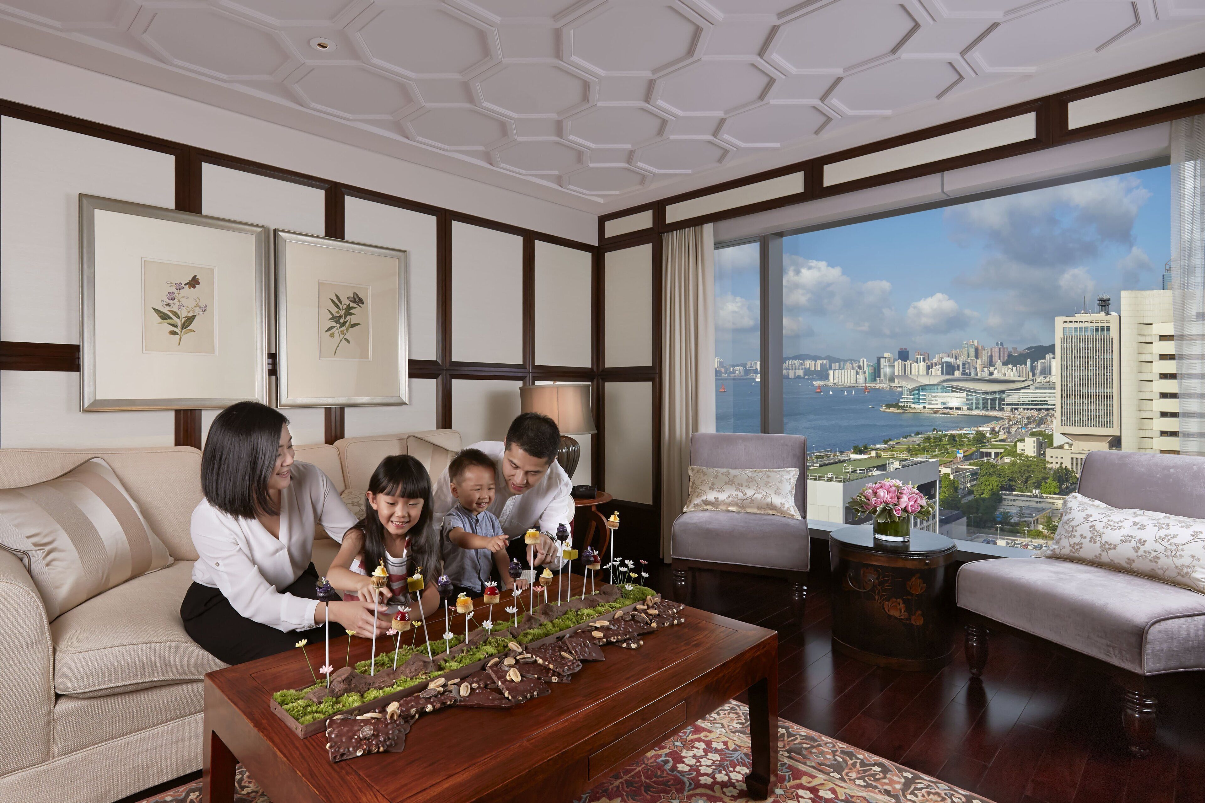 Un salon moderne avec vue sur la ville, une grande table basse en bois sur laquelle sont disposés des chocolats, et un coin salon confortable.