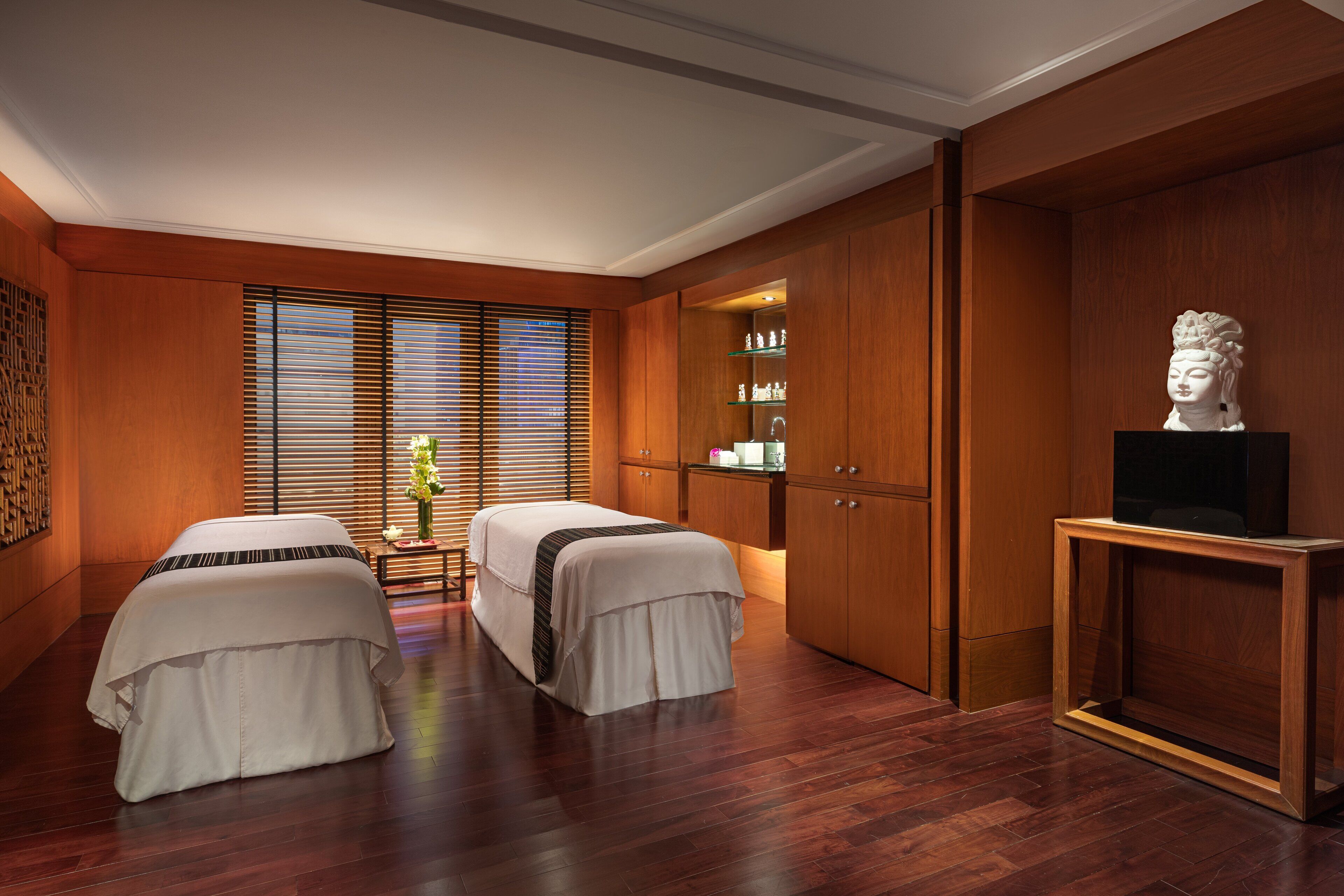 A room with two beds, wooden cabinets, a statue, and a TV on a stand.