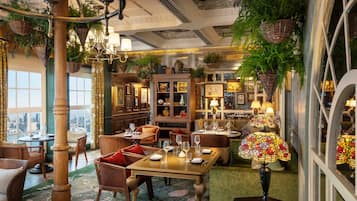 A restaurant with a view of the city, wooden furniture, hanging plants, and a chandelier.