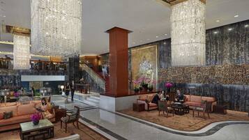 A spacious lobby with high ceilings, large chandeliers, a grand staircase, and a seating area with sofas and armchairs.