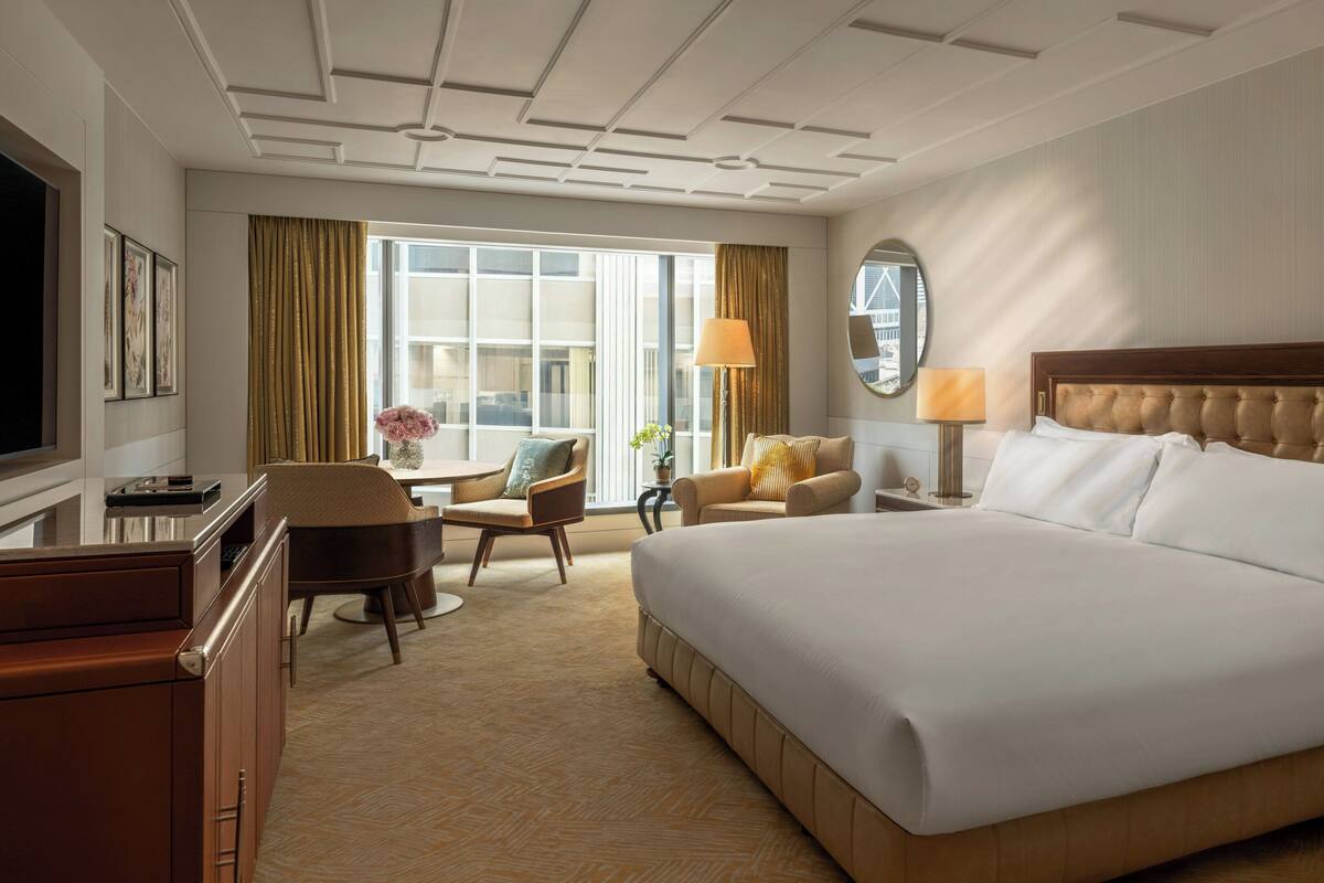 A hotel room with a large bed, a desk, a chair, a lamp, and a TV.