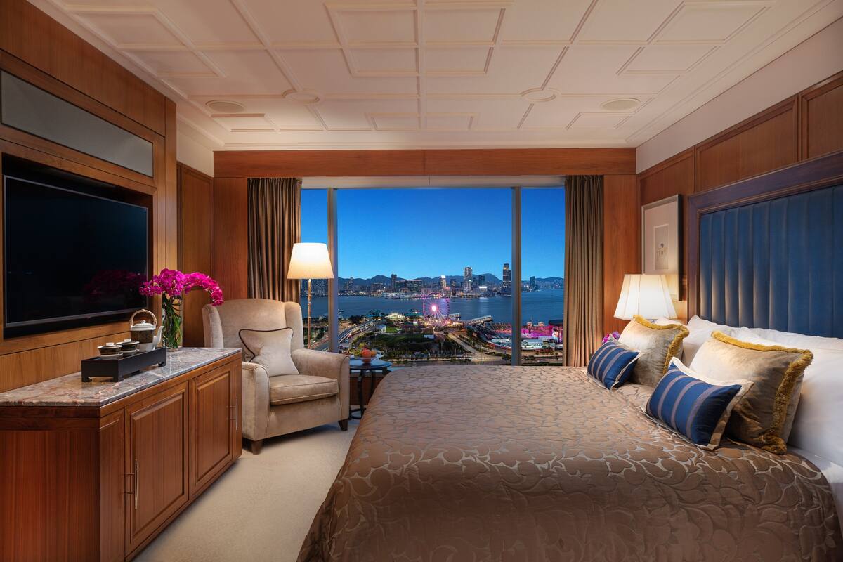 A hotel room with a large bed, a TV, a desk, and a view of a cityscape.