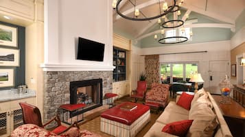 A spacious living room with a stone fireplace, comfortable seating, and a large chandelier.