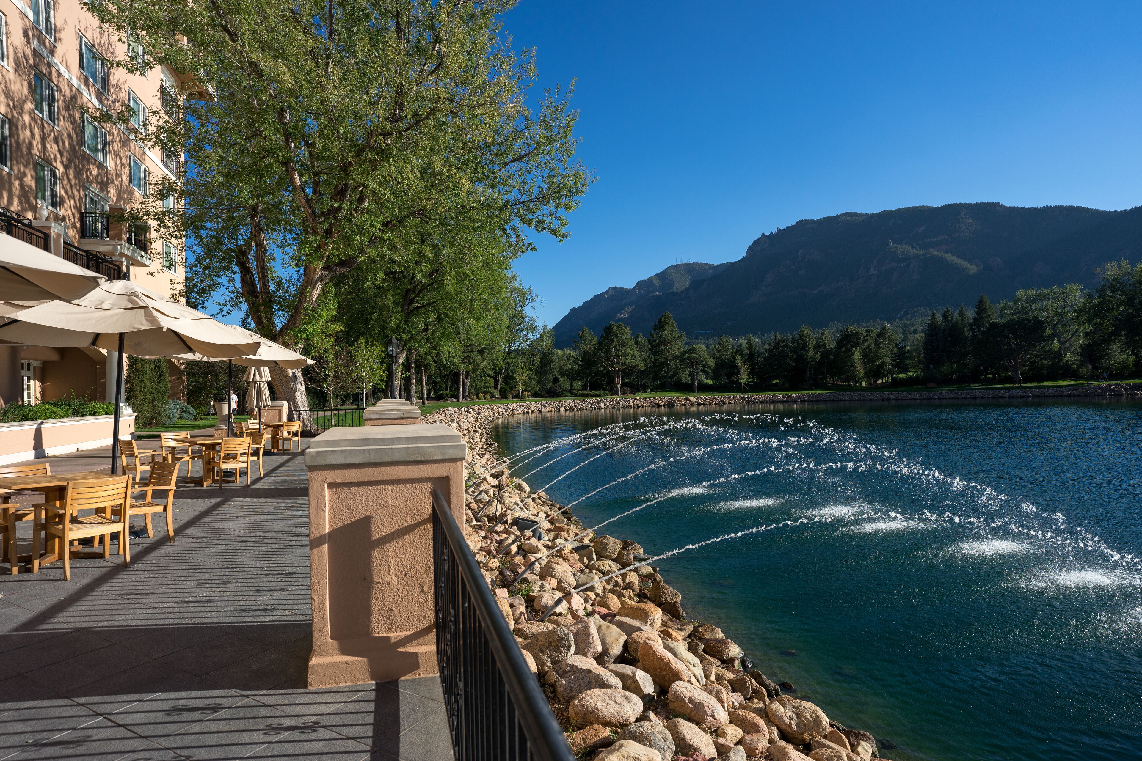 A riverside terrace with outdoor seating and a view of a mountain.