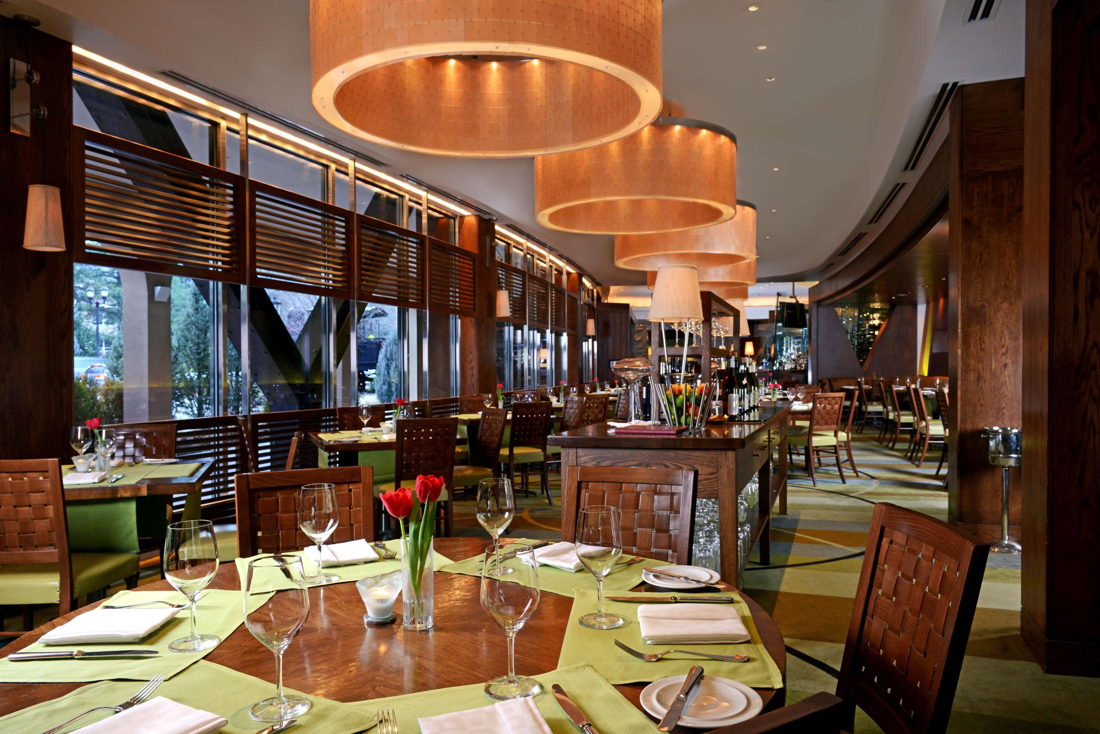 A restaurant with wooden tables, green cushioned chairs, and a large window with a view of trees.