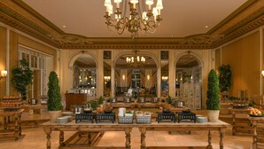 Eine imposante Lobby mit einem zentralen Tisch, aufwendigen Kronleuchtern und gespiegelten Wänden.