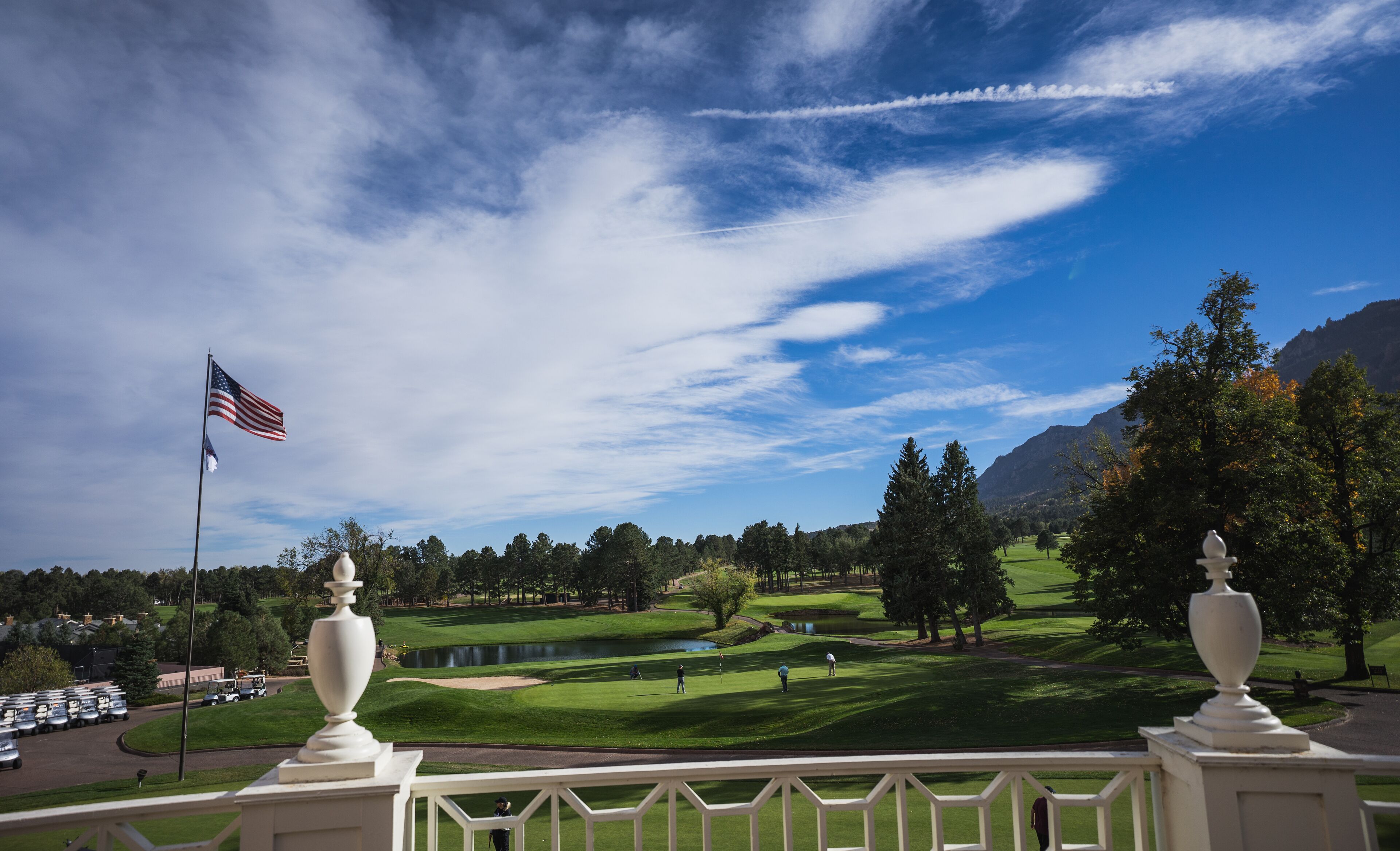 A golf course with a flag, trees, and a mountain in the background.