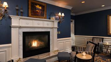 A room with a fireplace, striped upholstered chairs, a round table with a candle, and wall sconces.