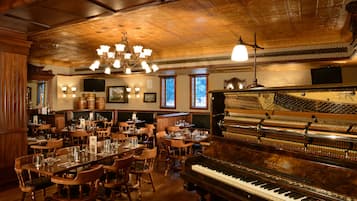 A restaurant with wooden interiors, a grand piano, and multiple dining tables and chairs.