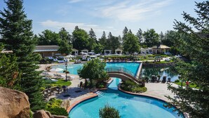 Ein Resort mit einem großen zentralen Pool, mehreren Liegebereichen und einer Brücke, die verschiedene Bereiche miteinander verbindet.